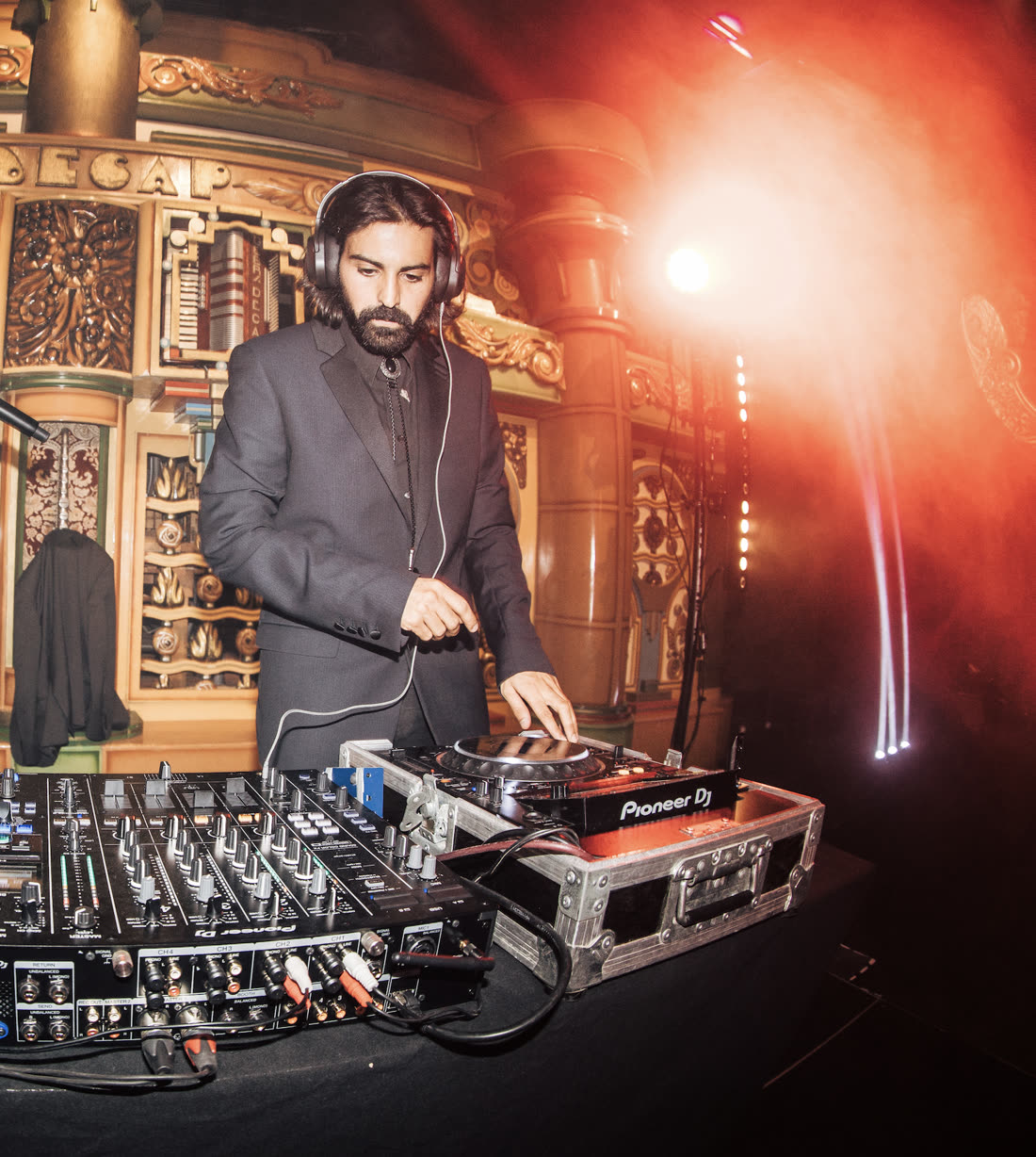 ZANAVI behind the decks in a dark suit, headphones on